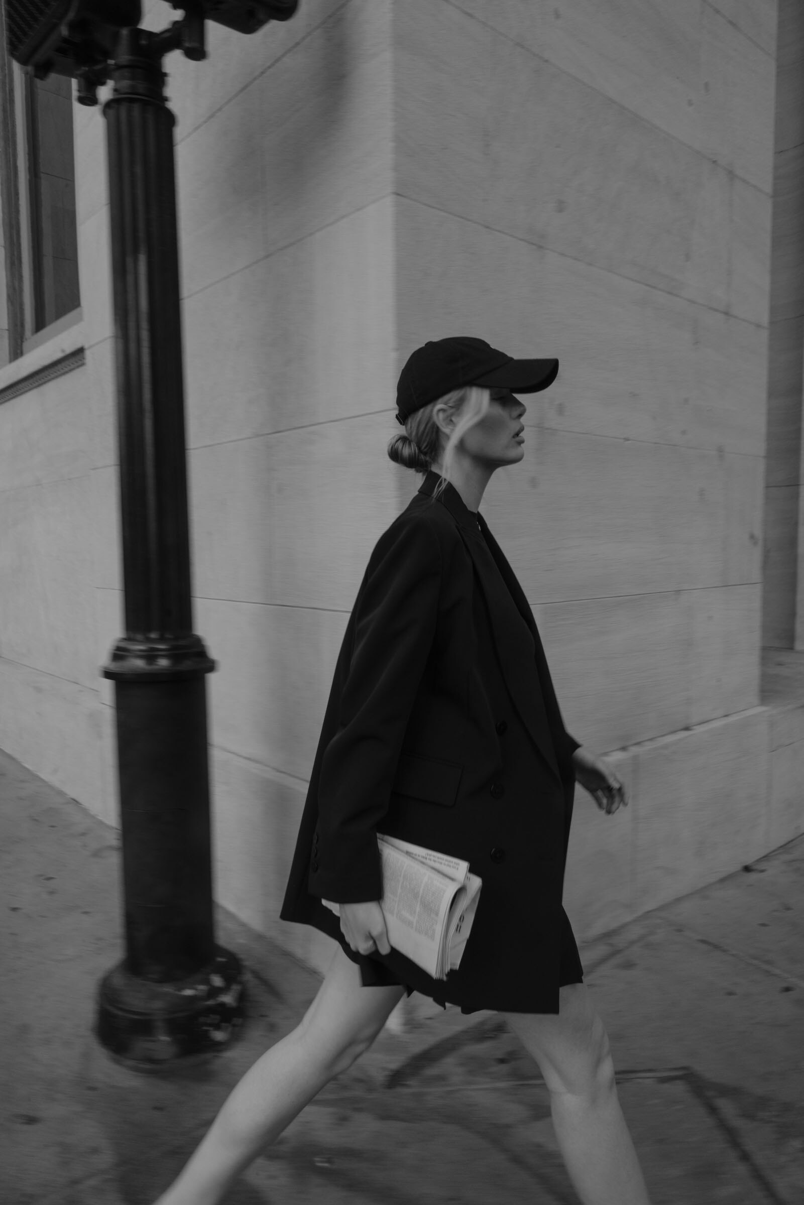 Fashionable woman walking around the corner of a building with a newspaper in hand.