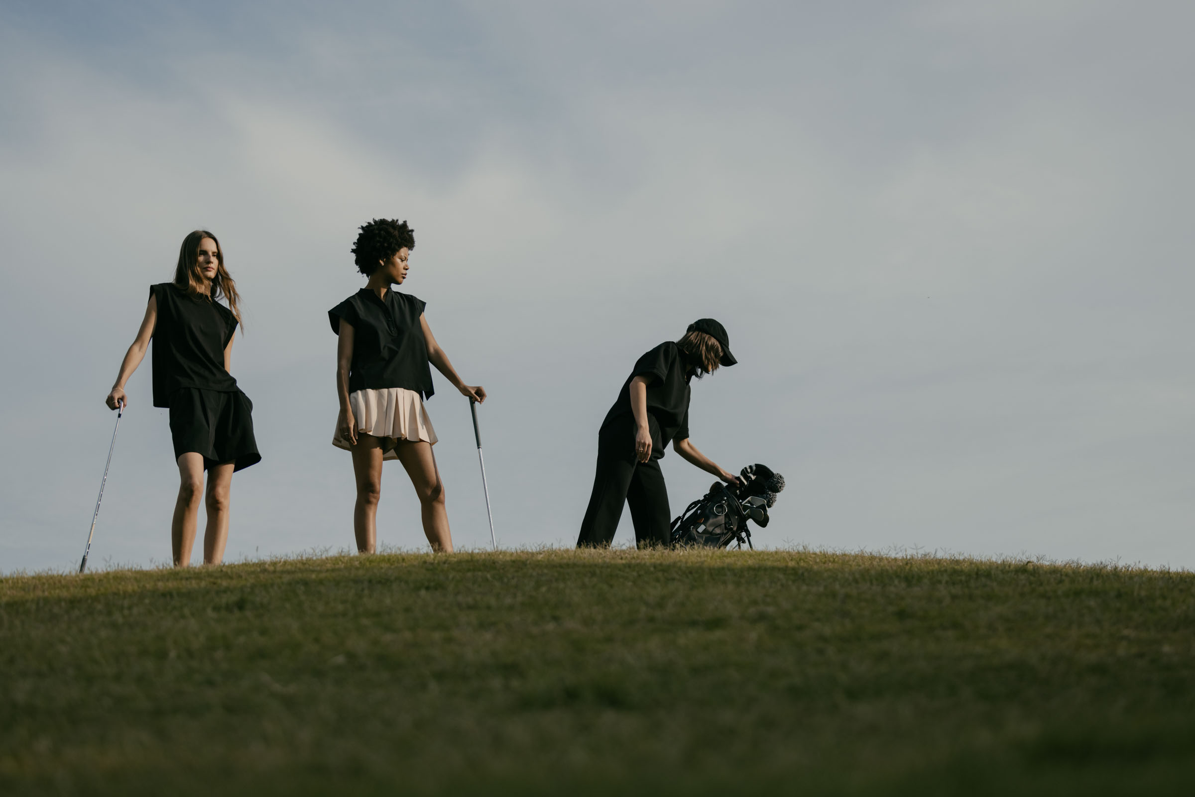 Three women walking on a golf course on a gloomy day.