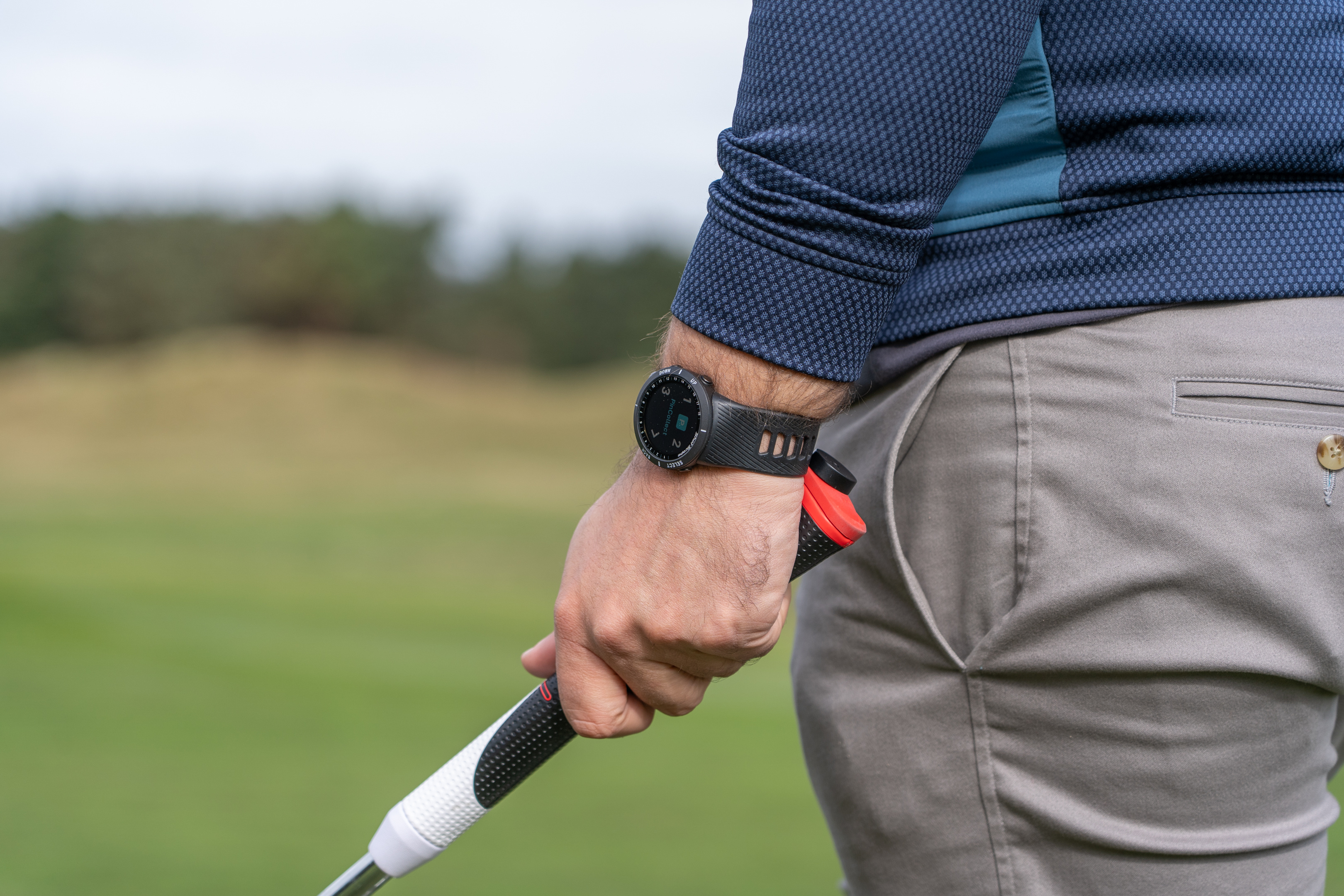 Man wearing a watch while gripping a golf club on a golf course.