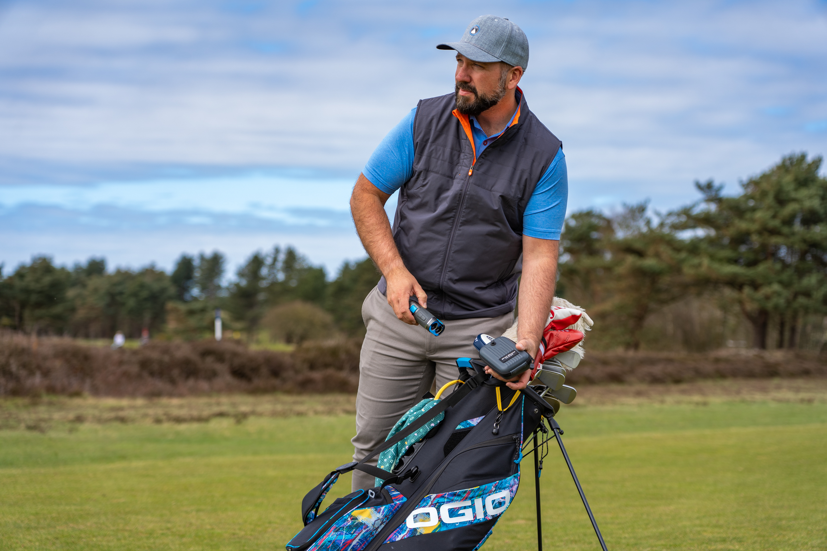 Man reaching for his range finder attached to his golf back on a golf course.