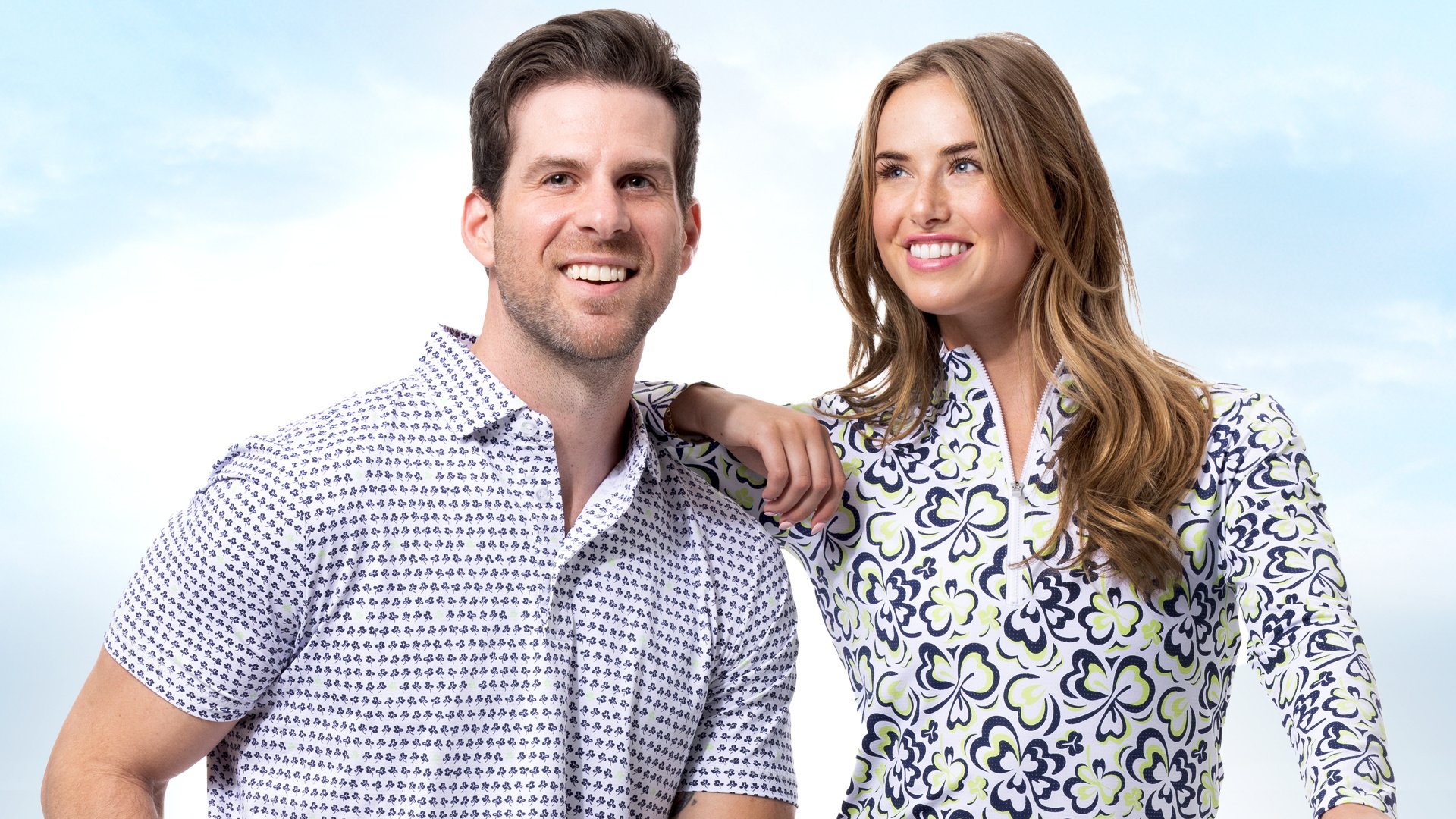 Man and a woman posing together wearing colorful athletic shirts with a light blue sky background.