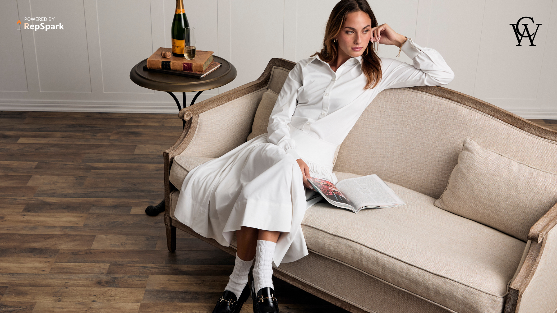 Woman sitting on a could in a white luxe outfit holding a book.