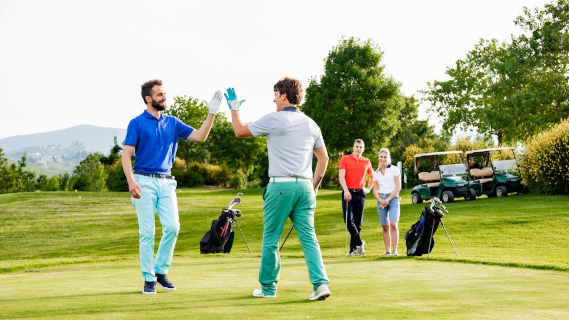 two men high fiving in golf apparel on grass