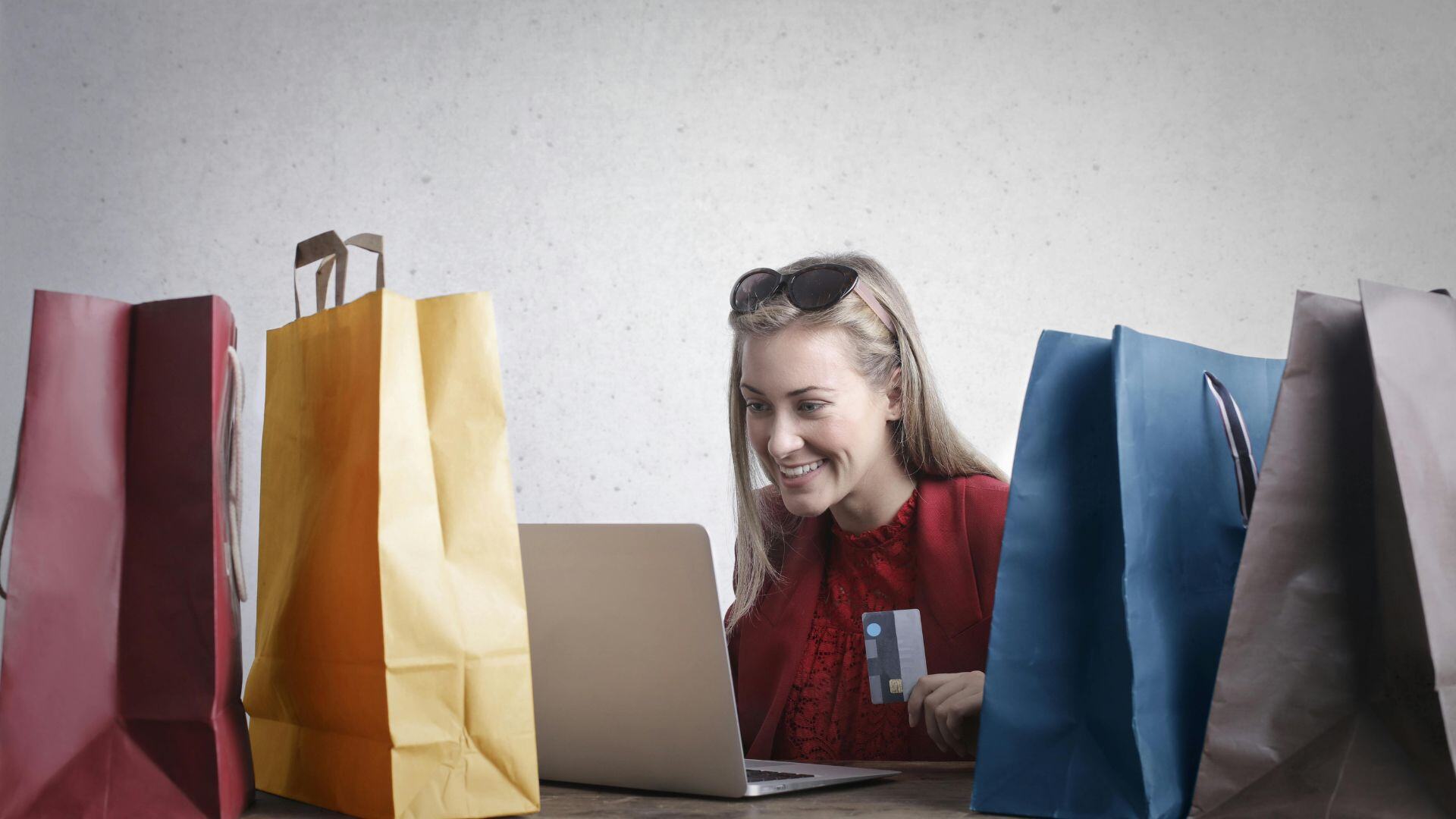 women looking at a laptop with a credit card in hand and shopping bags surrounding her 
